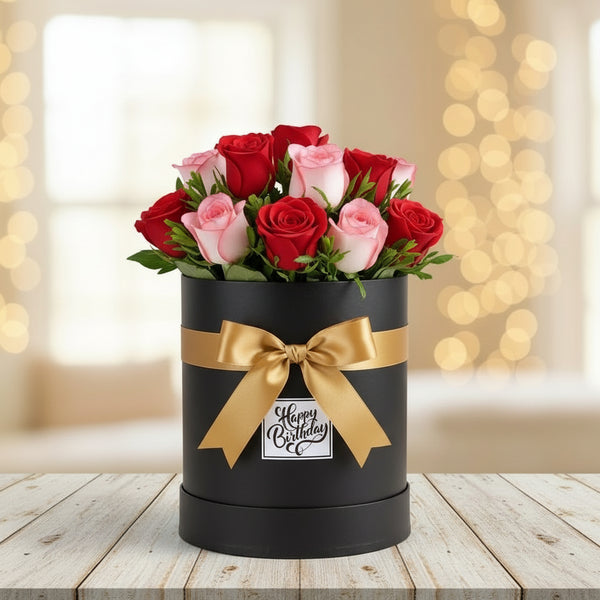 Black box with red and pink roses and a gold bow on a wooden table with a blurred background