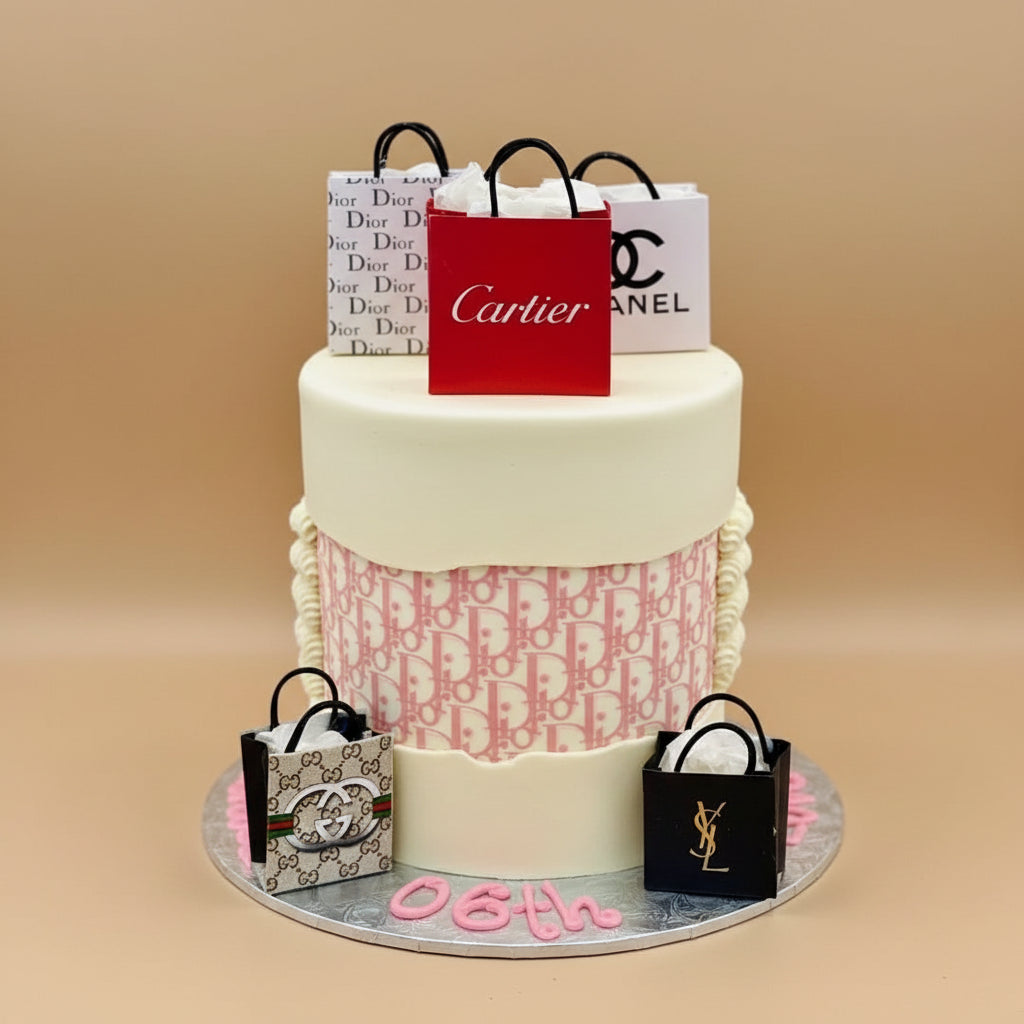 Pink cake with various luxury brand bags on a gray background