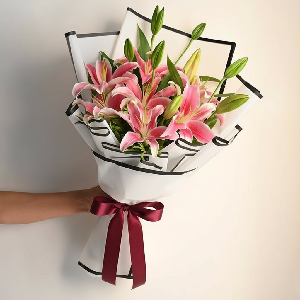 Bouquet of pink lilies wrapped in white paper with a black ribbon on a light background