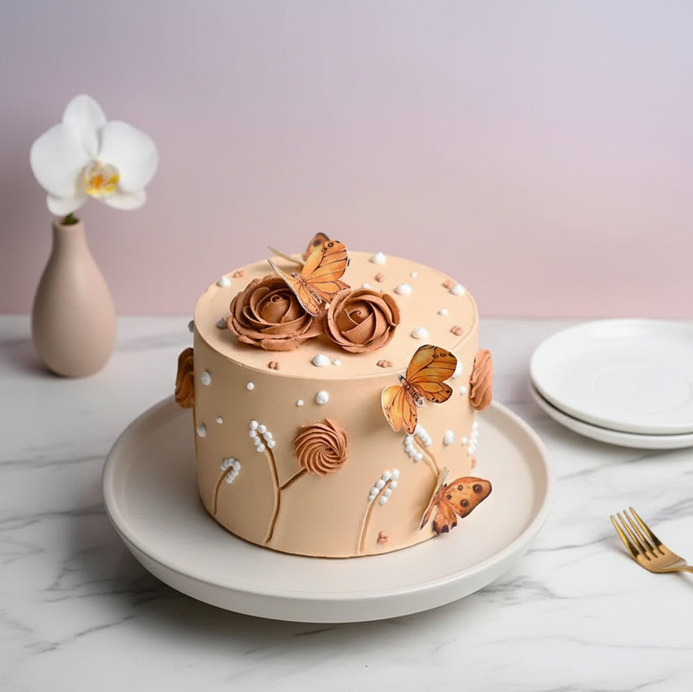Decorative cake with floral and butterfly designs on a marble surface with a vase and plates in the background.
