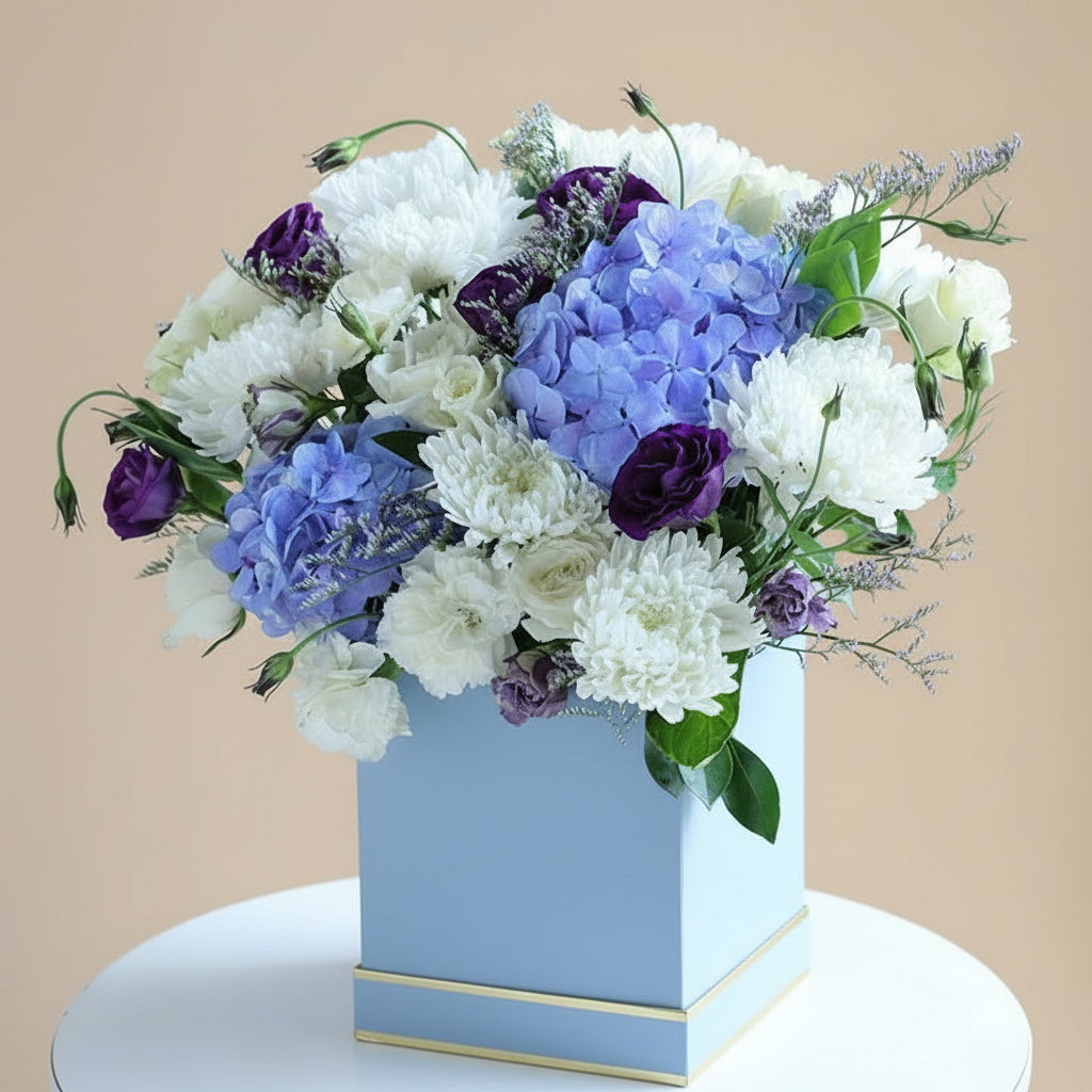 Bouquet of flowers in a blue box with  branding on a white surface.

